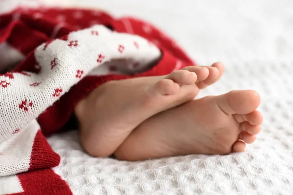 Los pies de un niño pequeño durmiendo debajo de la manta de punto rojo y blanco brillante Fotos de stock