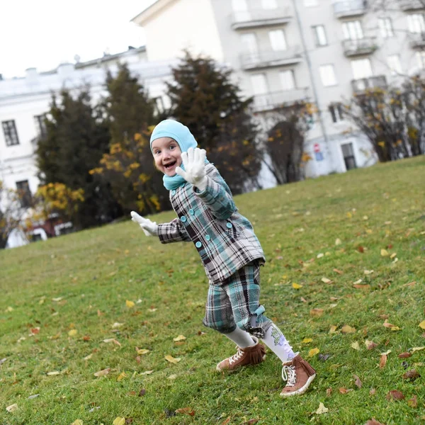 Ett foto av en skrattande sorglös liten flicka hoppa på en gräset i en park på hösten — Stockfoto