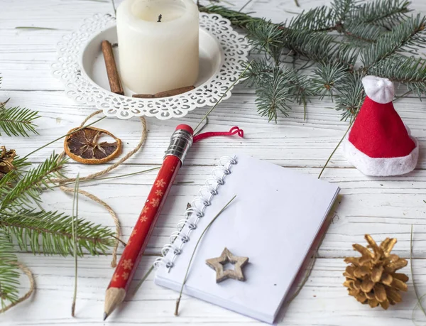 A festive winter mock up photo with a fir twigs, an opened note book, an old book, a pencil, cones, a candle and decation elements