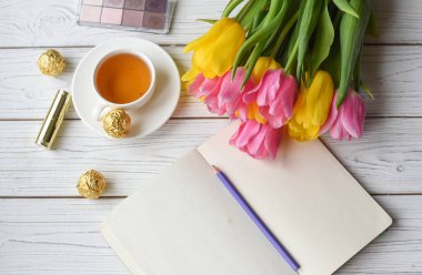 Bir bahar kavram - lale, çay, şeker, bir not defteri, mücevher, göz gölgeler paleti ve bir ruj bir buket temsil eden bir fotoğraf