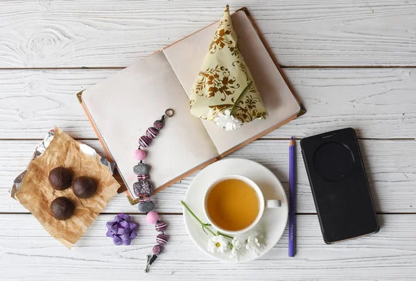 A photo representing a spring women inspiration: a cup of tea, a note book, several candies, a necklace nad flowers