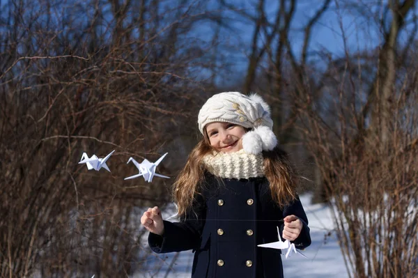 A positive photo representing a concept of coming spring - a smiling little girl in a park with paper cranes