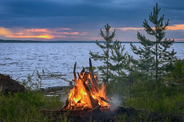 Big night bonfire by the river at sunset.