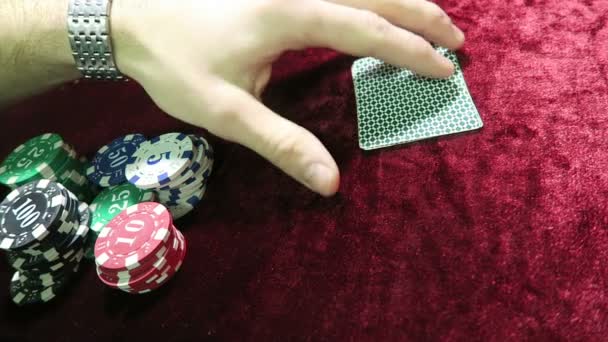 Игра в покер. человек смотрит на карты и делает ставку на все фишки. лежать вокруг чипсов. игра находится на красной ткани велюр стол . — стоковое видео