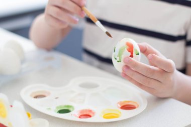 Bir çocuk suluboya ve guaj ile yumurta boyar Paskalya 'yı bekler ve oynar
