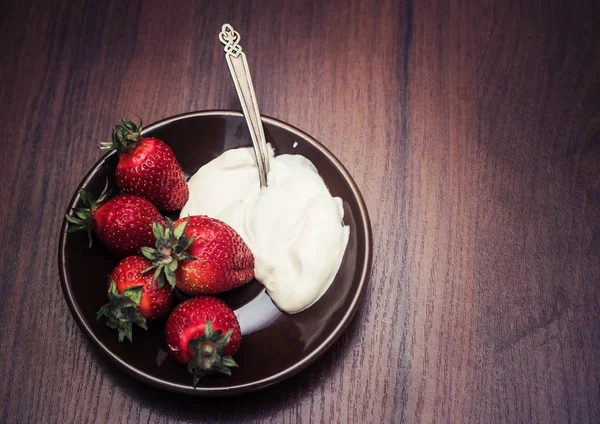 Strawberries with a spoon of cream on a plate — Stock Photo, Image