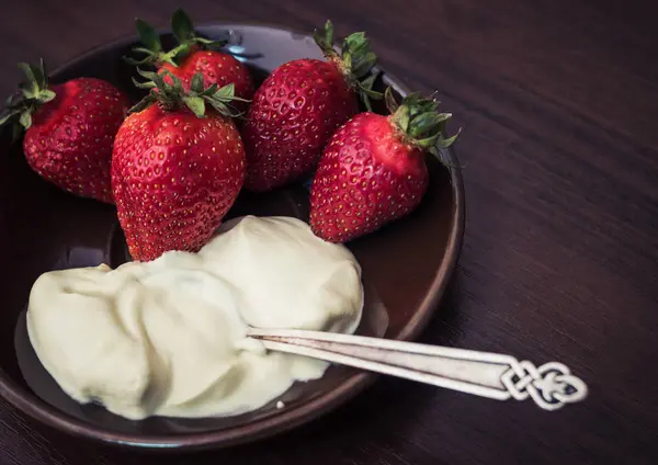 Strawberries with a spoon of cream on a plate — Stock Photo, Image