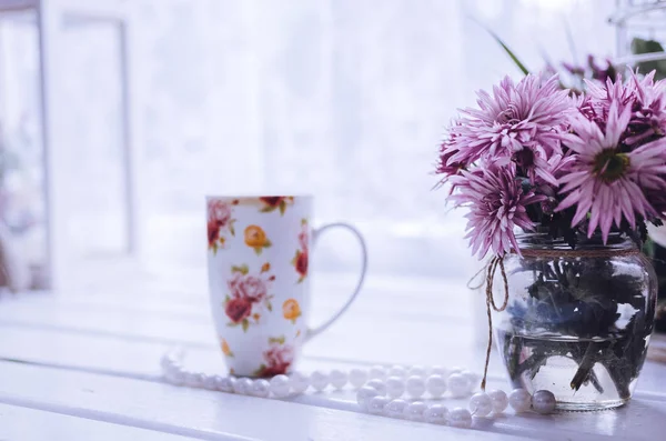 Flores cor de rosa com xícara de café ou chá perto da janela — Fotografia de Stock