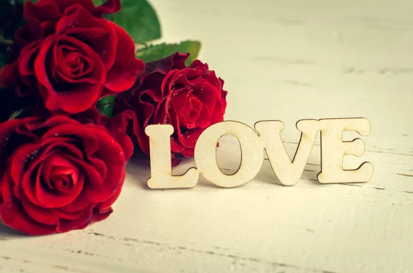 Λουλούδια κόκκινα τριαντάφυλλα με ξύλινη λέξη αγάπη — Φωτογραφία Αρχείου