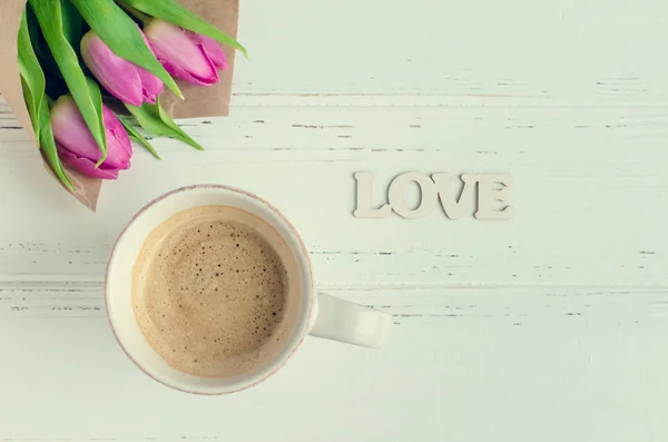 Xícara de café com buquê de tulipas rosa e palavra de madeira AMOR — Fotografia de Stock