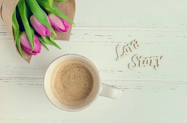 Kopp kaffe med bukett av rosa tulpaner och trä ord kärlekshistoria — Stockfoto