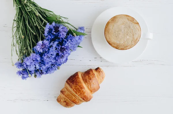 Xícara de café com buquê de flores de milho azul e croissant — Fotografia de Stock