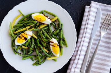 Taze yaz sıcak haşlanmış yumurta ve sos Balzamico glassa siyah taş zemin üzerine beyaz plaka ile pişmiş yeşil fasulye salatası. Sağlıklı beslenme. Vejetaryen yiyecekler kavramı. Üstten Görünüm.