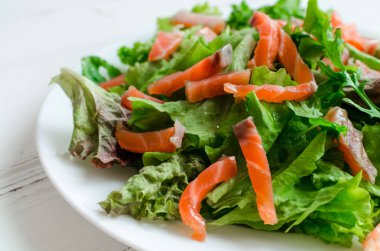 Yaprak sebze salatası salata ile mix, roka ve ahşap arka plan üzerinde beyaz tabakta somon füme. Sağlıklı beslenme kavramı.
