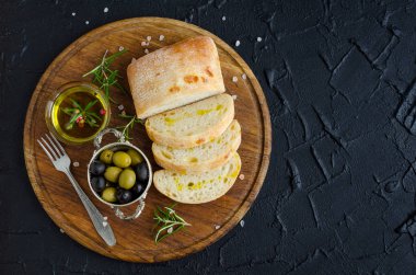 Mediterranean kümesi aperatifler. Yeşil ve Siyah Zeytin, zeytinyağı, otlar ve dilimlenmiş ciabatta ekmeği ahşap üzerinde taş koyu arka plan kurulu. İtalyan gıda kavramı. Üstten Görünüm. Kopya alanı.