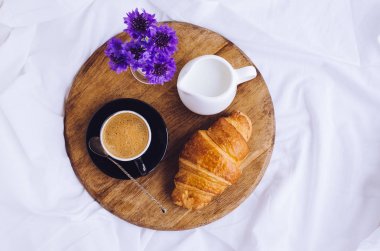 Romantik yaz odaya yatak, taze kruvasan ile tepsi, fincan sütlü kahve espresso ve mavi Peygamber buket. Günaydın kavramı. Yavaş hayattan zevk. Üstten Görünüm. Kopya alanı.