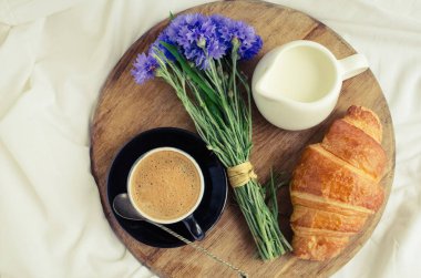 Romantik yaz odaya yatak, taze kruvasan ile tepsi, fincan sütlü kahve espresso ve mavi Peygamber buket. Günaydın kavramı. Yavaş hayattan zevk. Üstten Görünüm.