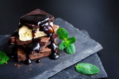 Çikolata koyu slate tahta üzerinde yeşil nane yaprakları ile eritilmiş çikolata ile siyah arka plan üzerine döktü kule yığını. Seçici odak, yakın. Kopya alanı.