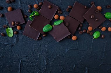 Kahve çekirdekleri şeker ile koyu çikolata, çikolata ile kaplı ve siyah arka plan üzerine yeşil nane yaprakları. Üstten Görünüm. Kopya alanı.