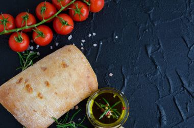 Geleneksel İtalyan ekmeği ciabatta taze pişmiş ekmek domates, biberiye, tuz, zeytinyağı ve zeytin ile siyah taş tabloda dilimlenmiş. Üstten Görünüm. Kopya alanı.
