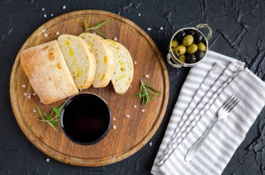 Şarap yemek saati ayarlayın. Bardak kırmızı şarap, yeşil ve siyah Akdeniz zeytin, dilimli ciabatta ekmeği ahşap tahta üzerinde taş koyu arka plan üzerinde. İtalyan gıda kavramı. Üstten Görünüm.