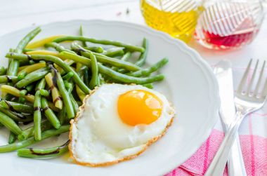 Pişmiş fasulye sosu Balzamico glassa ve kızarmış yumurta kırmızı peçete, bıçak ve çatal ile ahşap arka plan üzerinde beyaz plaka ile. Sağlıklı beslenme. Vejetaryen yiyecekler kavramı.