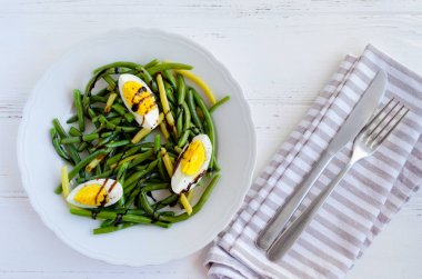 Haşlanmış yumurta ile pişmiş yeşil fasulye salatası sıcak ve Balzamico glassa gri peçete, bıçak ve çatal ile ahşap arka plan üzerinde beyaz tabak içinde sos. Sağlıklı beslenme. Vejetaryen yiyecekler kavramı. Üstten Görünüm.