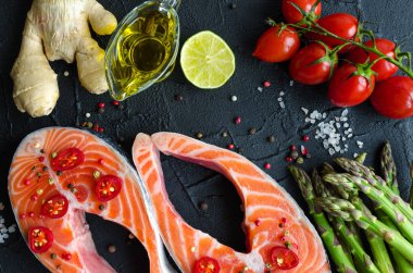 İki taze Çiğ somon biftek sebze ve baharatlar ile: kuşkonmaz, domates, zencefil, biber Mısır, tuz, biber biber, limon ve zeytin yağı siyah arka plan üzerine. Sağlıklı gıda diyet kavramı. Üstten Görünüm.