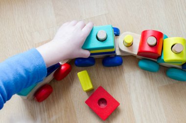Çocuk ahşap bir tren yerde topluyor. Oyuncak renkli detaylarını bebek dikkat çekmek. Oyun çocuğun parmakları bir motor becerilerini geliştirir. Üstten Görünüm.