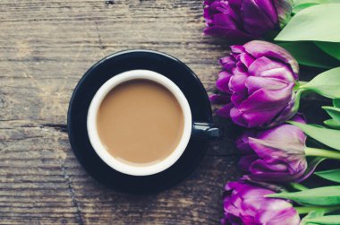 Bir fincan kahve süt ve eski ahşap zemin üzerine ultraviyole Lale buketi. Kahvaltı anneler günü, Sevgililer günü veya kadın gün. Romantik sabah kavramı. Üstten Görünüm. Düz yatıyordu. Tonlu görüntü.