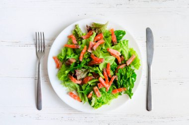 Yaprak sebze salatası salata ile mix, roka ve bıçak ve çatal Beyaz ahşap zemin üzerinde bir plaka üzerinde somon füme. Sağlıklı gıda kavramı. Üstten Görünüm.