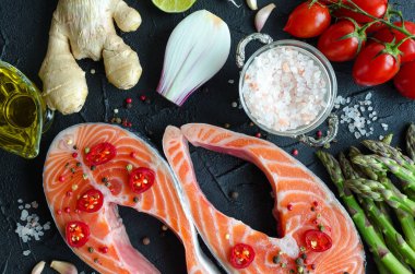 İki taze Çiğ somon biftek sebze ve baharatlar ile: kuşkonmaz, domates, zencefil, biber Mısır, tuz, biber, soğan, limon ve zeytin yağı siyah arka plan üzerine. Sağlıklı gıda diyet kavramı. Üstten Görünüm.