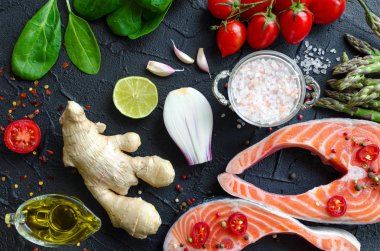 İki taze Çiğ somon biftek ile kuşkonmaz, ıspanak, sarımsak, domates, zencefil, biber Mısır, tuz, biber, soğan, limon ve zeytin yağı siyah arka plan üzerine. Sağlıklı gıda diyet kavramı. Üstten Görünüm.