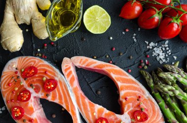 İki taze Çiğ somon biftek sebze ve baharatlar ile: kuşkonmaz, domates, zencefil, biber Mısır, tuz, biber biber, limon ve zeytin yağı siyah arka plan üzerine. Sağlıklı gıda diyet kavramı. Üstten Görünüm.