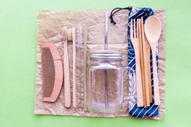 Sıfır atık. Bambu çatal bıçak takımı ve diş fırçaları, cam kavanozlar, yeşil arka planda metal ve bambu pipetleri. Sürdürülebilir yaşam. Eko dostu plastik eşyalar. Üst görünüm.