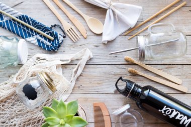 Sıfır atık. Pamuk torbaları, bambu çatal bıçaklar, diş fırçaları, cam kavanozlar ve ahşap zemin üzerinde metal su şişesi. Sürdürülebilir yaşam. Eko dostu plastik eşyalar. Üst görünüm.