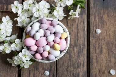 Paskalya kompozisyonu, pastel renkte mini çikolata yumurtaları ve kırsal ahşap arka planda beyaz kiraz çiçekleri. Mutlu Paskalyalar. Üst görünüm.