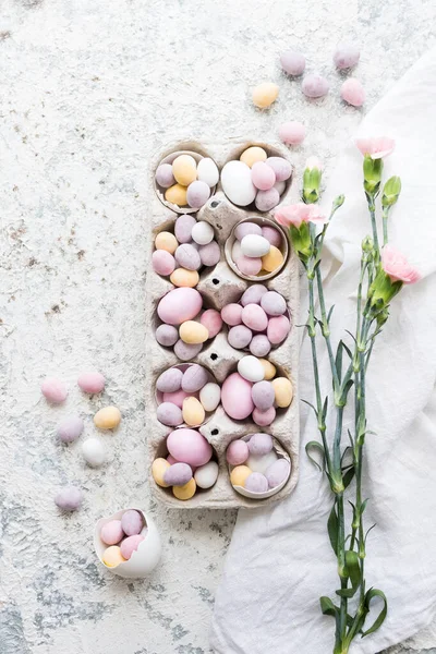 Easter composition with mini chocolate eggs in pastel colors and pink flowers on grey concrete background. Happy Easter Holidays. Top view. Copy space.