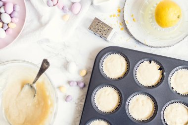 Hazırlık süreci, beyaz mermer arka planda mini çikolatalı yumurtalarla süslenmiş Paskalya kekleri. Mutlu Paskalyalar. Üst görünüm.