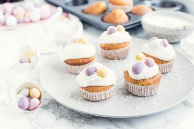 Beyaz mermer arka planda mini çikolatalı yumurtalarla süslenmiş Paskalya kekleri. Mutlu Paskalyalar..