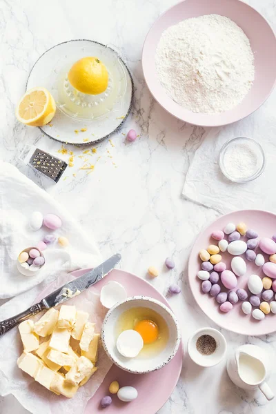 Paskalya pastası hazırlama süreci ya da beyaz mermer arka planda çikolatalı yumurtalarla süslenmiş küçük kekler. Paskalya pastası konsepti. Üst Manzara. Boşluğu kopyala.