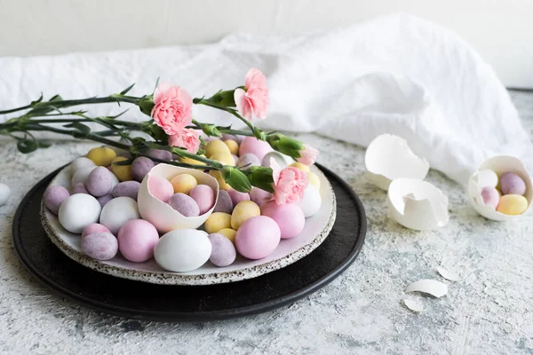Easter composition with mini chocolate eggs in pastel colors and pink flowers on grey concrete background. Happy Easter Holidays.