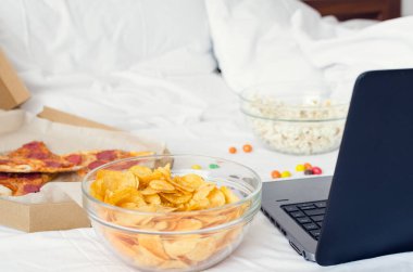 Corona virüsü - evde kalmak (kendini izole etmek). Sağlıksız yaşam tarzı olan ev karantinası. Laptop ve fast food ile vakit geçirmek. Fast food atıştırmalıkları: pizza, patlamış mısır, patates cipsi ve bilgisayar.