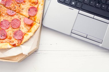 Evde çalışmak ve yemek teslimatı. Sağlıksız yaşam tarzı olan ev ofisi. Laptop ve fast food ile vakit geçirmek. Fast food pizza ve bilgisayar masada. Üst Manzara. Boşluğu kopyala.