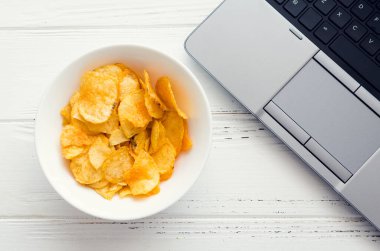 Evde çalışmak ve aperatifler. Sağlıksız yaşam tarzı olan ev ofisi. Laptop ve fast food ile vakit geçirmek. Patates cipsi ve bilgisayar masada. Üst görünüm.