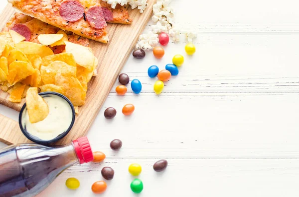 Fast food and unhealthy eating concept. Close up of fastfood snacks: pizza, popcorn, potato chips and candies. Assortment of carbohydrates products bad for skin, heart and teeth. Top view. Copy space.