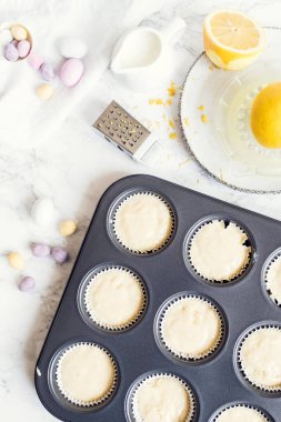 Hazırlık süreci, beyaz mermer arka planda mini çikolatalı yumurtalarla süslenmiş Paskalya kekleri. Mutlu Paskalyalar. Üst görünüm.