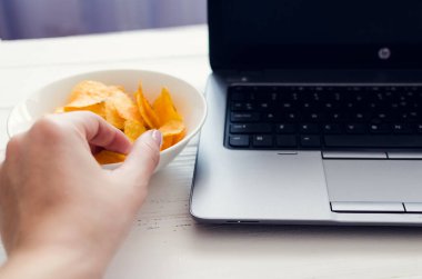 Evde çalışmak ve aperatifler. Sağlıksız yaşam tarzı olan ev ofisi. Laptop ve fast food ile vakit geçirmek. Patates cipsi ve bilgisayar masada..