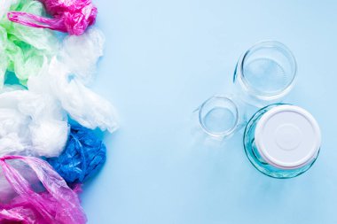Birçok tek kullanımlık plastik torba mavi arka planda yeniden kullanılabilir cam kavanozlara karşı. Sıfır atık. Sürdürülebilir yaşam, plastiksiz konsept. Eko dostu plastik eşyalar. Üst görünüm.