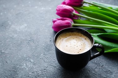 Bir fincan köpüklü kahve ve siyah arka planda pembe laleler. Anneler Günü 'nde, Sevgililer Günü' nde ya da Kadınlar Günü 'nde kahvaltı. Romantik sabah konsepti. Boşluğu kopyala.